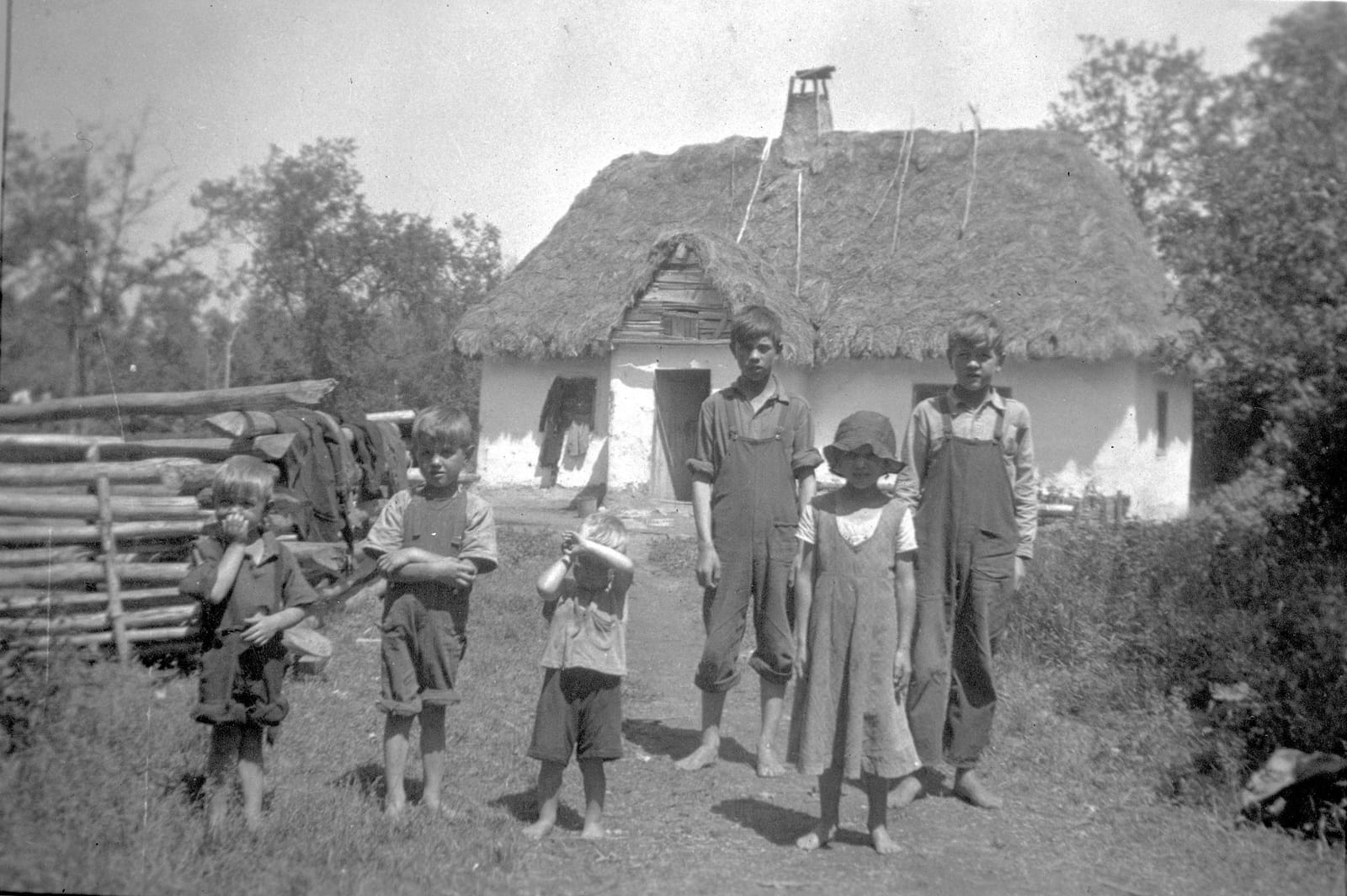 Five barefoot children standing in front of a small whitewashed thatched house with a pole roof, Athabasca, Alberta, 1920.
