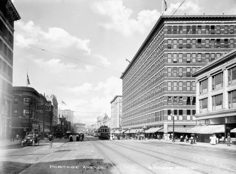 Portage Avenue in Winnipeg looking east, with streetcar tracks, the Eaton’s store on the right, pedestrians, and an early automobile.