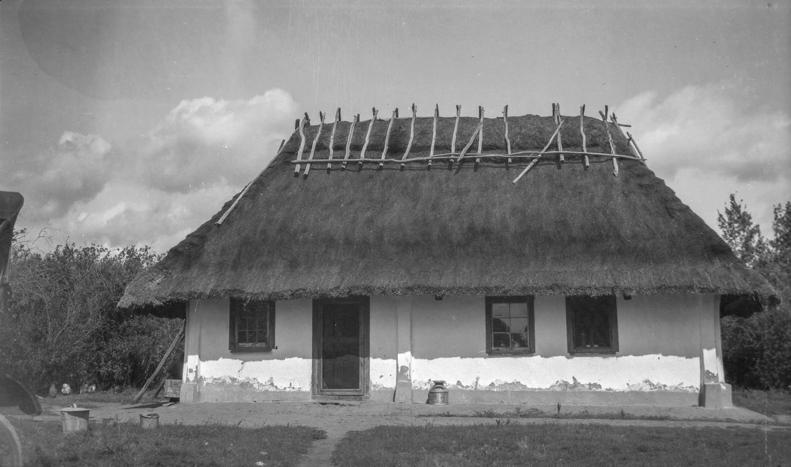 A whitewashed cottage with a thick thatched roof weighted by poles, two windows, and a central door, Smoky Lake, Alberta, 1922.